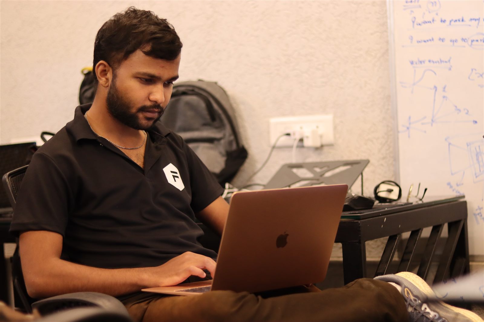 Ayush Rai working on a laptop in a workspace, with a whiteboard of notes behind him.